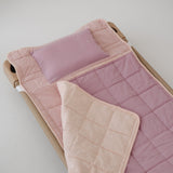 A soft purple and dusty pink stripe quilted daycare bedding nap mat with a soft peach underside on quilt. It has a built in matching pillowcase, pillow insert, name tag and carry handle. The daycare bedding nap mat is laid out on a daycare stacker bed frame against a white background.