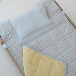 A light blue and white gingham quilted daycare bedding nap mat with soft yellow on the underside of the blanket. It has a built in matching pillowcase, pillow insert, name tag and carry handle. The daycare bedding nap mat is laid out on a daycare stacker bed frame against a white background.
