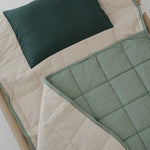 A olive green and beige stripe quilted daycare bedding nap mat with a dark green pillowcase attached. It has a built in matching pillowcase, pillow insert, name tag and carry handle. The daycare bedding nap mat is laid out on a daycare stacker bed frame against a white background.
