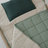 A olive green and beige stripe quilted daycare bedding nap mat with a dark green pillowcase attached. It has a built in matching pillowcase, pillow insert, name tag and carry handle. The daycare bedding nap mat is laid out on a daycare stacker bed frame against a white background.