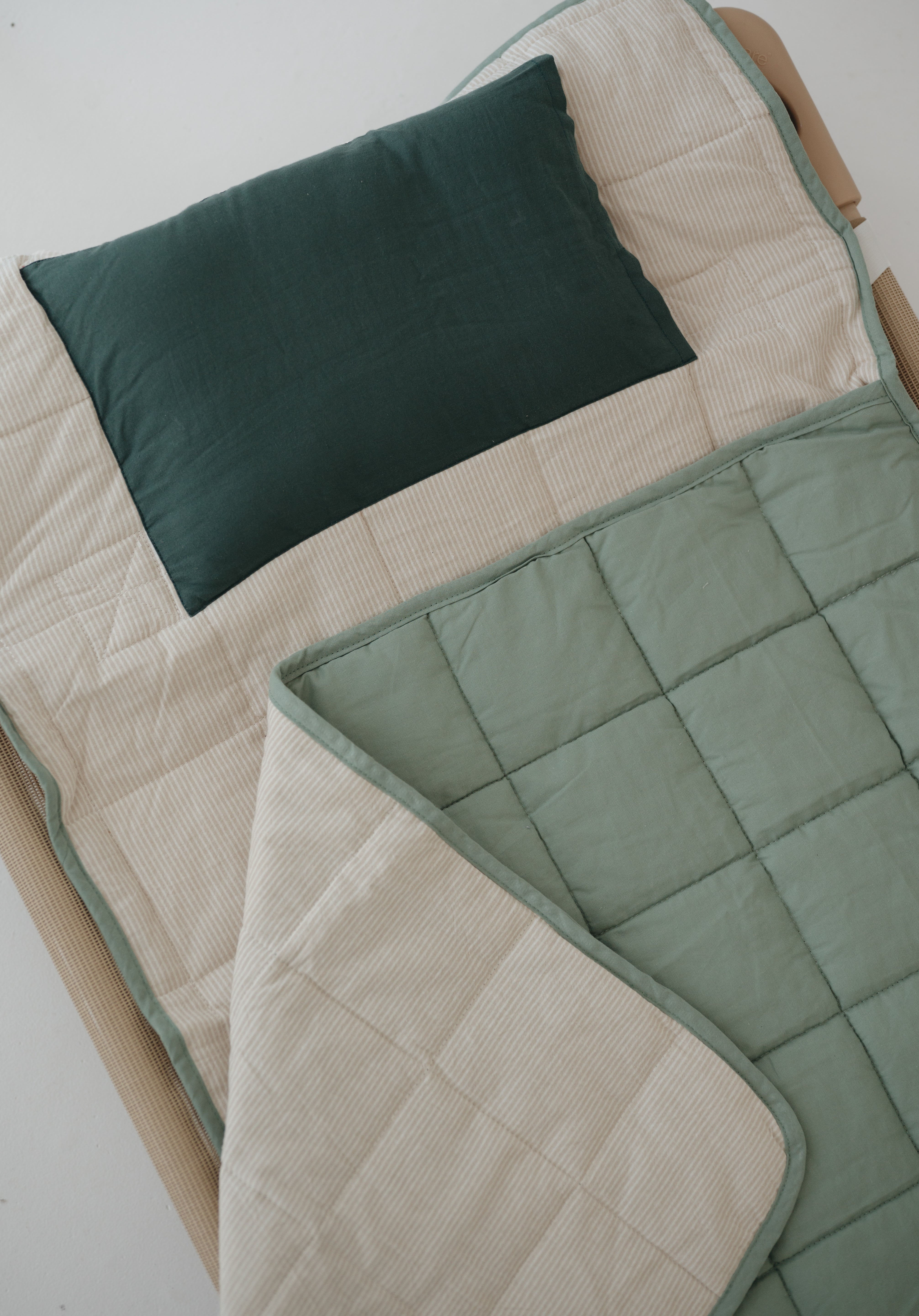 A olive green and beige stripe quilted daycare bedding nap mat with a dark green pillowcase attached. It has a built in matching pillowcase, pillow insert, name tag and carry handle. The daycare bedding nap mat is laid out on a daycare stacker bed frame against a white background.