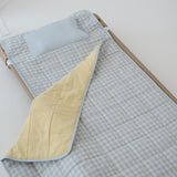 A light blue and white gingham quilted daycare bedding nap mat with soft yellow on the underside of the blanket. It has a built in matching pillowcase, pillow insert, name tag and carry handle. The daycare bedding nap mat is laid out on a daycare stacker bed frame against a white background.