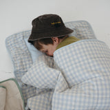A light blue and white gingham quilted daycare bedding nap mat with soft yellow on the underside of the blanket. It has a built in matching pillowcase, pillow insert, name tag and carry handle. The daycare bedding nap mat is laid out on the floor being used a sleeping bag for a child and photographed with a white background.