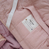 A soft purple and dusty pink stripe quilted daycare bedding nap mat with a soft peach underside on quilt. It has a built in matching pillowcase, pillow insert, name tag and carry handle. The daycare bedding nap mat is laid out showing the name tag, carry handle and elastic straps that help secure it to a daycare stacker bed and rolled up when not in use.