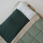 A olive green and beige stripe quilted daycare bedding nap mat with a dark green pillowcase attached. It has a built in matching pillowcase, pillow insert, name tag and carry handle. The daycare bedding nap mat is laid out on a daycare stacker bed frame against a white background showing the pillow insert that is included.