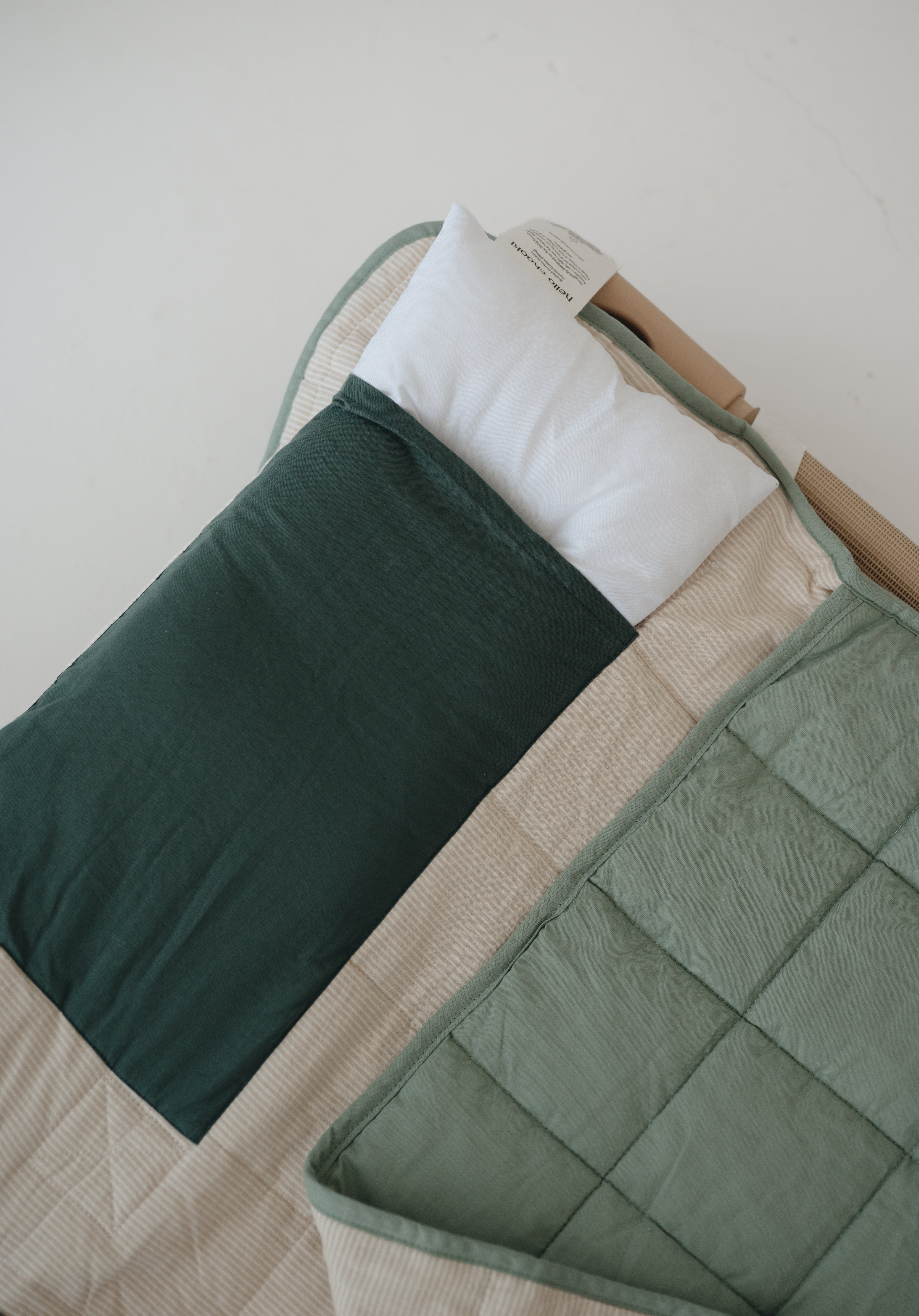 A olive green and beige stripe quilted daycare bedding nap mat with a dark green pillowcase attached. It has a built in matching pillowcase, pillow insert, name tag and carry handle. The daycare bedding nap mat is laid out on a daycare stacker bed frame against a white background showing the pillow insert that is included.