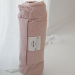 A soft purple and dusty pink stripe quilted daycare bedding nap mat with a soft peach underside on quilt. It has a built in matching pillowcase, pillow insert, name tag and carry handle. The daycare bedding nap mat is rolled up against a white background.