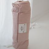 A soft purple and dusty pink stripe quilted daycare bedding nap mat with a soft peach underside on quilt. It has a built in matching pillowcase, pillow insert, name tag and carry handle. The daycare bedding nap mat is rolled up against a white background.