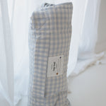 A light blue and white gingham quilted daycare bedding nap mat with soft yellow on the underside of the blanket. It has a built in matching pillowcase, pillow insert, name tag and carry handle. The daycare bedding nap mat is rolled up showing how it is packed away not in use and photographed against a white background.