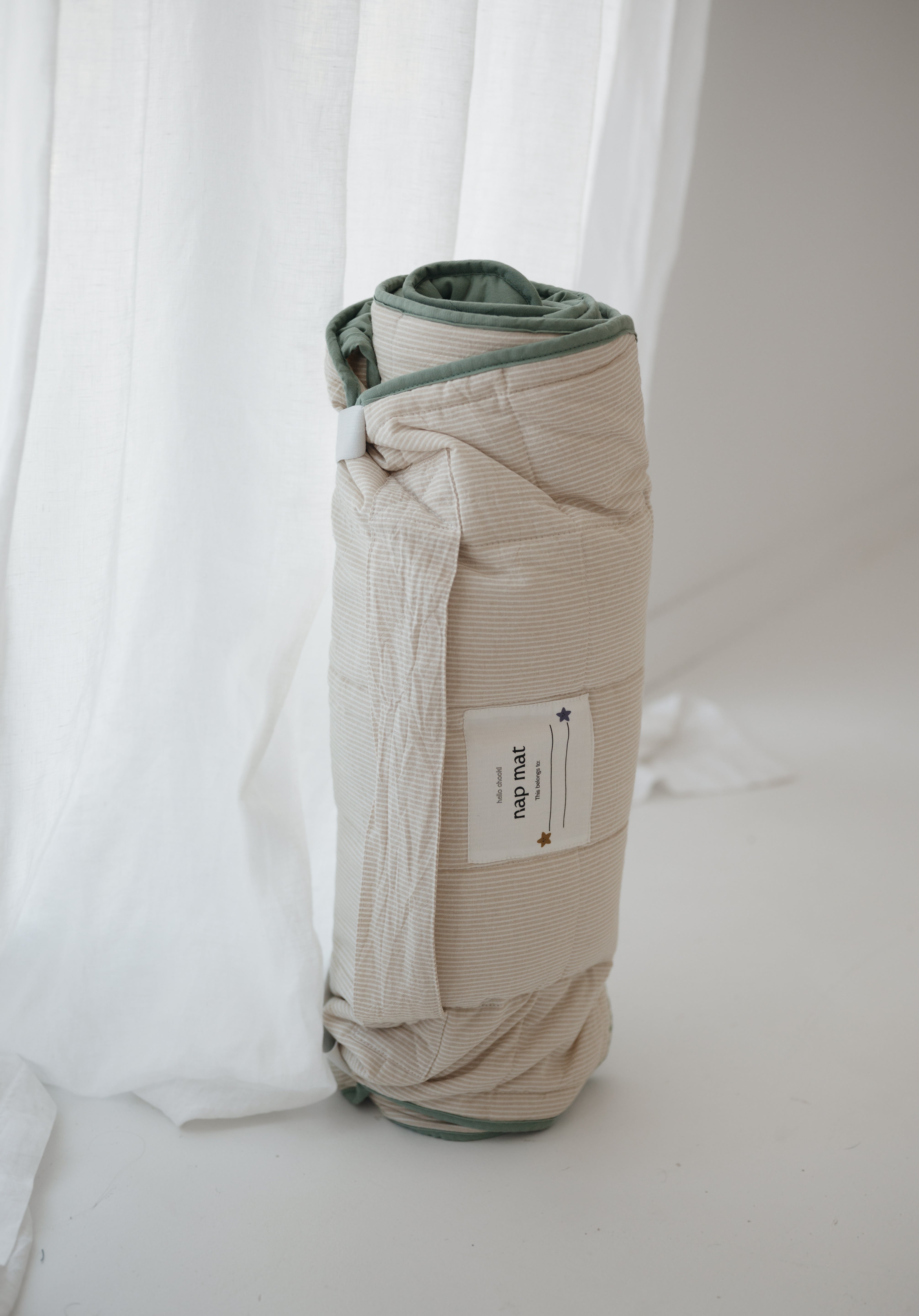A olive green and beige stripe quilted daycare bedding nap mat with a dark green pillowcase attached. It has a built in matching pillowcase, pillow insert, name tag and carry handle. The daycare bedding nap mat is rolled up against a white background.