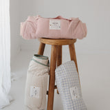 A olive green and beige stripe quilted daycare bedding nap mat with a dark green pillowcase attached. It has a built in matching pillowcase, pillow insert, name tag and carry handle. The daycare bedding nap mat is rolled up against a timber stool next to alternative prints from the daycare bedding nap mat collection, photographed with a white background.