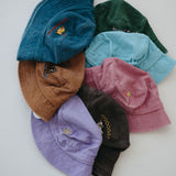 A group of seven toddler daycare washed cotton bucket hats in various colours (light blue, green, brown, dark blue, pink, purple, dark brown) arranged in a circle on a plain white background.