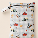 A rectangle PUL fabric daycare wet bag  with a zipper closure and a button loop strap, printed with a hand sketched farm-themed pattern on a light blue and white gingham background. The print includes red barns, tractors, cows, chickens, and other farm animals with a girl and a horse and a boy with his dog. Shown against a solid light beige background.