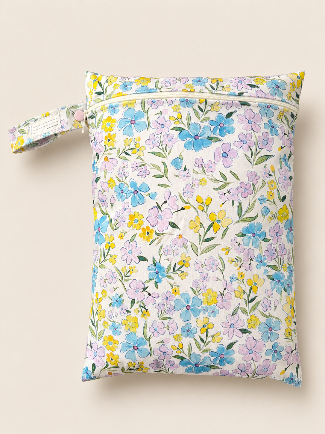 A PUL material zippered wet bag with a colourful hand sketched floral print on a cream background, featuring a matching fabric wrist strap with button closure, shown against a solid light beige background. Floral colours a soft purple, soft pink and soft yellow with soft green stems.