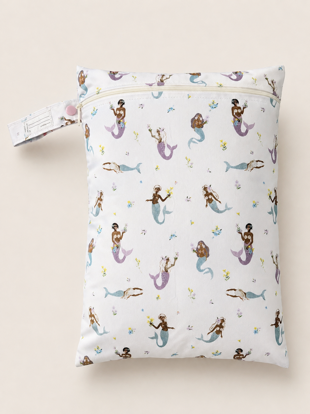 A rectangle zippered daycare wet bag  featuring a repeating pattern of mermaids in various colours of purple and blue on a white background, shown against a light beige backdrop. Also features a pastel purple button for convenience of attaching to any bag or pram and a name tag to help alleviate any daycare mixups.