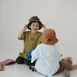 Two toddlers sitting on a white floor wearing a light brown washed cotton daycare bucket and a dark brown washed cotton daycare bucket with oversized t-shirts in a minimalist studio setting. One child wears an olive green t-shirt and a dark brown hat, while the other wears a light blue t-shirt  a light brown hat.